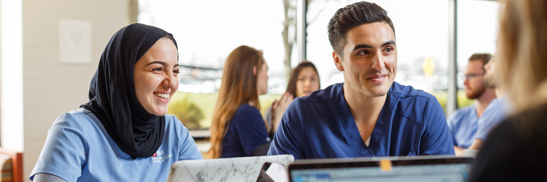 Groups of dentistry students work on their laptops at tables.
